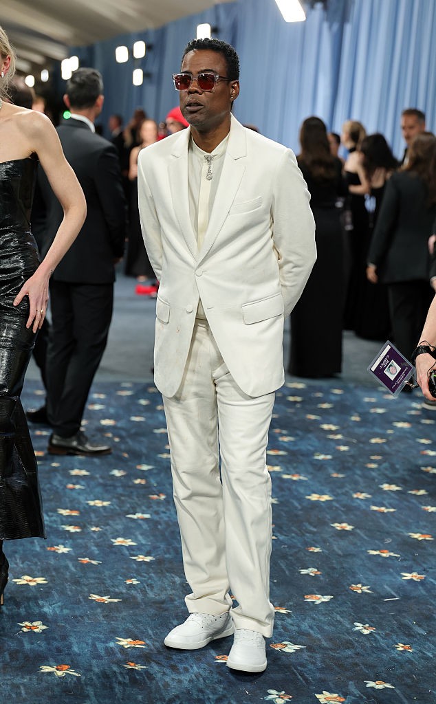 Chris Rock – Gabriela Hearst: Chris Rock a letisztult elegancia híveként jelent meg a Met-gálán egy hófehér Gabriela Hearst öltönyben, amely a minimalizmus és a precíz szabás tökéletes példája volt. A fehér sportcipő és a tónusban tartott ing laza, mégis összehangolt stílust sugallt, miközben a napszemüveg és az ezüst nyaklánc diszkréten emelte ki a megjelenés dandy-faktorát. Rock megmutatta: a tailoring nem csak extravagancia lehet – néha épp a visszafogottság az, ami igazán ütős hatást kelt.