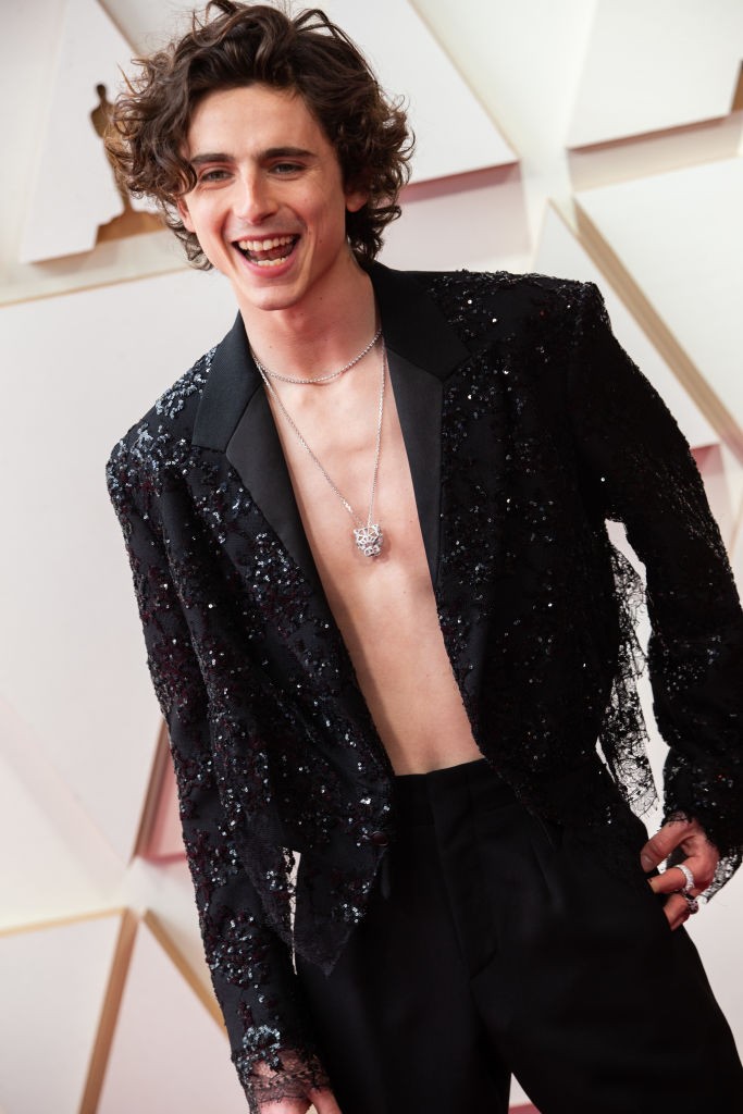 Timothée Chalamet többször is hátat fordított a maszkulin vonalnak. Egy fekete flitteres Louis Vuitton öltönyben érkezett a 2022-es Oscar-gálára, a különleges darab Nicolas Ghesquière tervező munkája, ami a Louis Vuitton 2022-es tavaszi-nyári női kollekciójába tartozik. Az öltönyt elegáns szabása és letisztult vonalvezetése miatt bárki felveheti, ezzel pedig Chalamet bebizonyította, hogy a divat nem a nemek meghatározásáról szól. Ami a Cartier ékszereket illeti, a fehérarany gyűrű és nyaklánc volt az outfit stílusos megkoronázása.