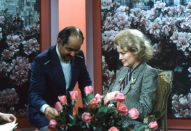 Az NBC stúdiójában készült ezt a pillanatkép, 1980 decemberében, a Today Show felvételén. A háttérben virágos díszlet, előtte rózsák – Grace Kelly pedig egy apró, természetes gesztus közben látható.