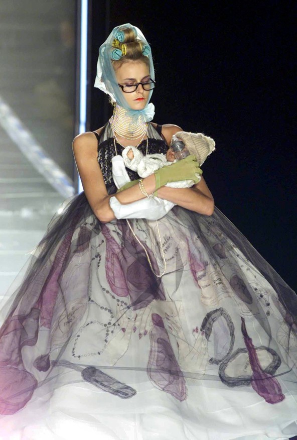 Galliano szinte mindenből tud inspirációt meríteni, és mindig átértelmezve, de részletgazdagon jeleníti meg a világban látottakat a kollekcióiban. Itt az anyaság kicsit ironikus, de rendkívül elegáns változatban jelenik meg.