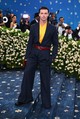 Patrick Schwarzenegger – Balmain: Patrick Schwarzenegger megjelenése a Met-gála vörös szőnyegén egyszerre volt nosztalgikus és ultramodern. A sötét csíkos Balmain öltöny a klasszikus tailoring vonalait idézte, de a sárga selyeming, a piros bőröv és a hozzá illő clutch hatásos színkontrasztja minden klasszicizmust felrobbantott. A bő szabású nadrág és a kifinomult részletek remekül egyensúlyozták a maszkulin alapokat és a divat iránti nyitottságot. 