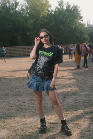 A farmer miniszoknya újra hódít – ráadásul stílusosabb, mint valaha. Bő pólóval, láncos kiegészítőkkel és szegecselt bakanccsal párosítva tökéletes választás a laza, mégis vagány megjelenéshez. A szettet az apró napszemüveg teszi teljessé, mintha a fesztiválozó épp egy zenekar backstage-éből lépett volna elő.
