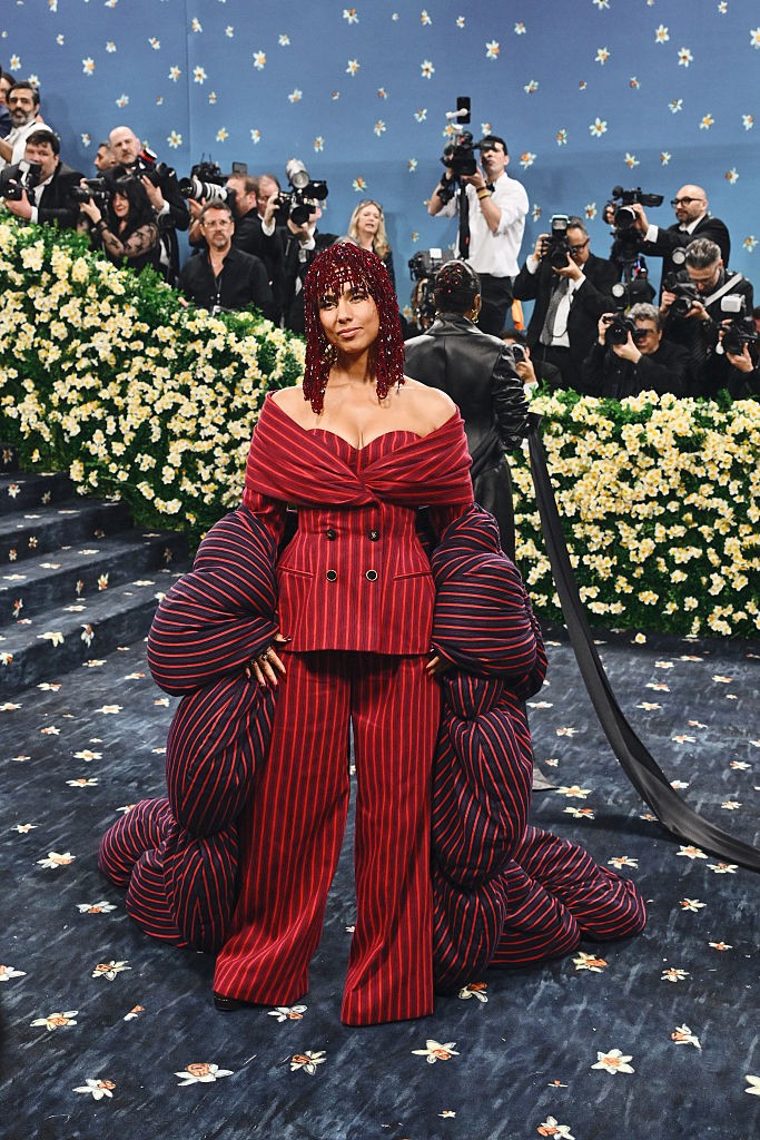 Alicia Keys – Moncler: Az énekesnő nem csupán belebújt egy öltönybe, hanem újra is gondolta. A vörös és sötétkék csíkos, túlméretezett Moncler szett egyszerre idézi a klasszikus dandy stílust és formabontóan írja újra a szabászat szabályait. A puffos ujjakból épített drámai uszály futurisztikus eleganciát csempész az összeállításba, miközben a flitteres, gyöngyökkel díszített hajdísz koronaként zárja a látványt. Keys megjelenése szó szerint és átvitt értelemben is súlyt ad a tailoring új definíciójának.