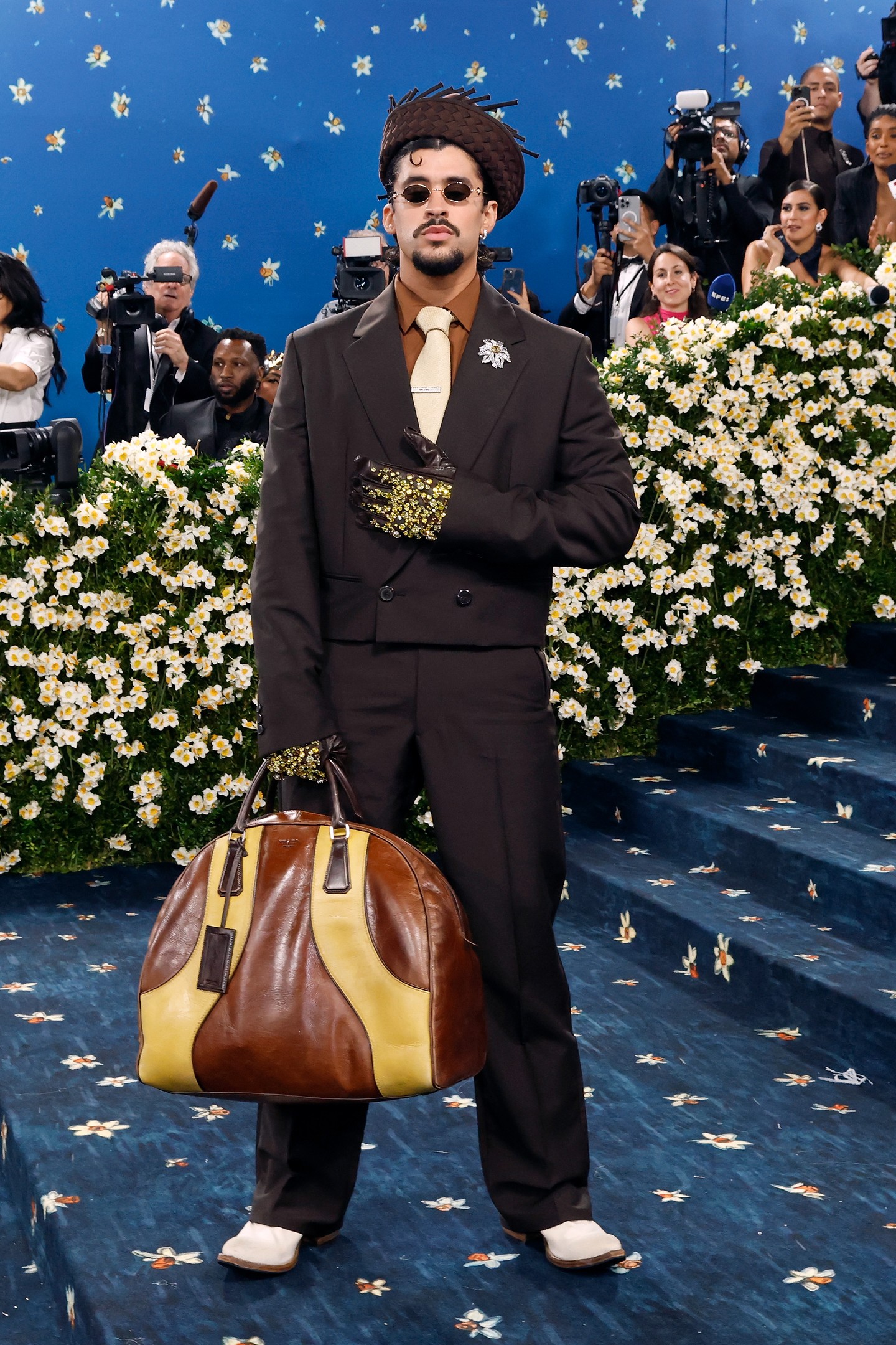 Bad Bunny lenyűgöző stílusban jelent meg a Met-gálán, tovább erősítve divatdiktátor státuszát. A legmegdöbbentőbb kiegészítője? Egy nagy táska az oldalán. A zenész egy Prada öltönyt viselt, míg fején egy hagyományosan pálmalevelekből szőtt puerto ricói De León szalmakalap volt. Nyakkendője ugyanebből az anyagból készült, beépítve megjelenésébe egy csipetnyi örökséget.