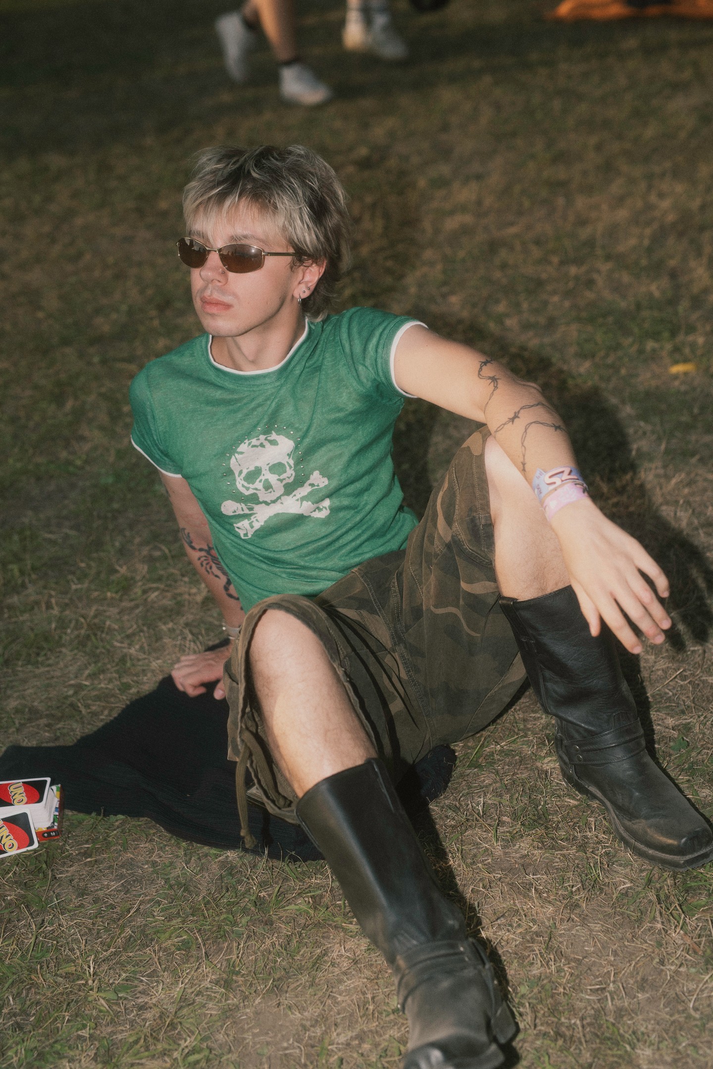 Az alternatív, punk–grunge ihletésű fesztiválstílus idén erőteljesen jelen volt a Sziget Fesztiválon. A zöld, kopott hatású póló a korszak DIY- és rockos grafikai trendjeit idézi, míg a terepmintás, térdig érő nadrág a military-esztétika irányába tolja az összhatást.