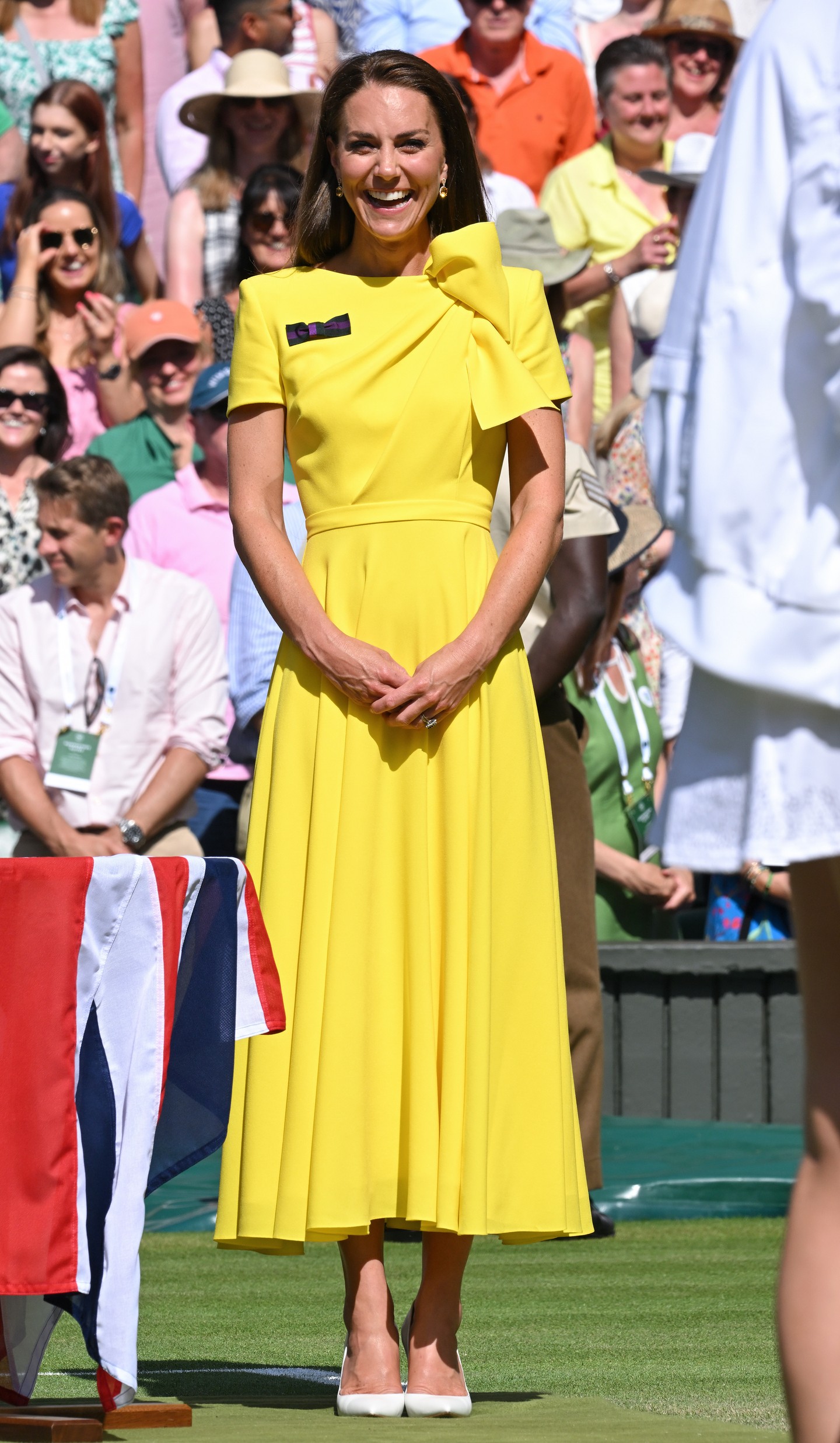 Katalin hercegné ragyogó napsárga Roksanda-ruhájával igazi színfoltja volt a 2022-es wimbledoni női döntőnek – ugyanebben a ruhában korábban a karibi körúton is láthattuk. A rövid ujjú, strukturált vállú, oldalt masnival díszített maxi ruha önmagában is figyelemfelkeltő volt, de a kiegészítők tették igazán teljessé a megjelenést. A szett összértéke mintegy 4 417 font, vagyis körülbelül 2 millió forint. Az összeállítás részét képezte egy fehér Gianvito Rossi magassarkú, Bvlgari napszemüveg, LK Bennett kalap, valamint Kiki McDonough citrin- és gyémánt fülbevalója, amely önmagában is közel 1,1 millió forintot ér.
