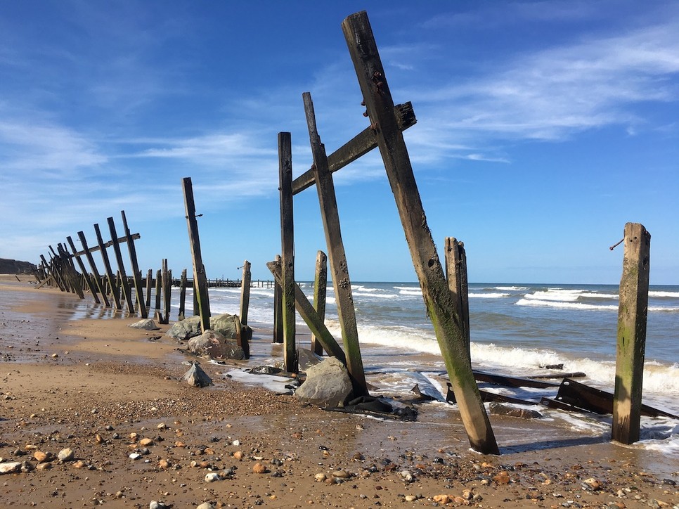 Happisburgh partján az erózió erősödése egybeesik a partok előtt évtizedekkel ezelőtt emelt fa védfalak pusztulásával (fent). Ma már sziklafal tompítja a hullámokat. A kövek között felfedezhetők az egykori föld alatti csővezetékek cementágyának maradványai (lent). (Fotók: a szerző)