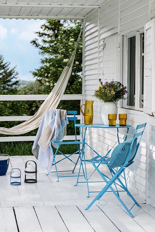 Indiánnyár a verandán, teraszon – élénk kék kerti bútorok, virágcsokor és függőágy, amelyek tökéletesen megteremtik a nosztalgikus, mégis modern hangulatot