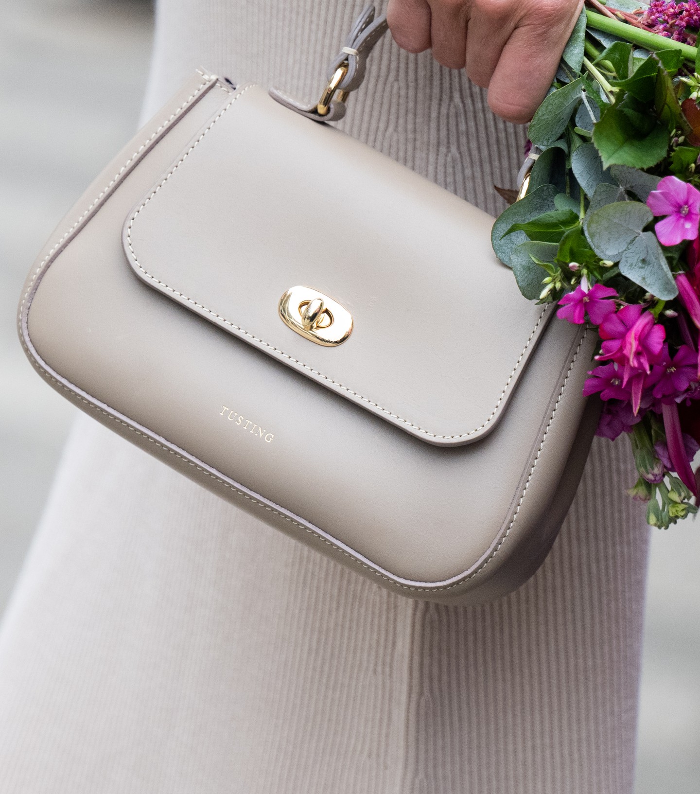 Jobb kezében a Tusting luxus bézs kézitáskáját vitte magával