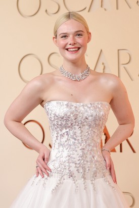 A ruha dekoltázsán és a szoknya alsó részén ezüst virághímzés díszelgett, melynek jelentése is volt. A fűzőben és a Cartier-ékszerekben is visszaköszönő finom akácmotívumot gyermekkori otthona ihlette. „Gyerekkoromban az otthonomban volt egy akácfa, ami tavasszal virágzott” – mesélte Fanning. „Emlékszem, azt gondoltam, hogy a legszebb dolog az, amikor a szirmok lehullanak, és felhőt hoznak létre a földön.” Burton és a Givenchy csapata ezt az emléket hímzéssé alakította: minden apró szirmot kézzel varrtak selyemszálakkal kék, rózsaszín, ezüst és lila árnyalatokban. 