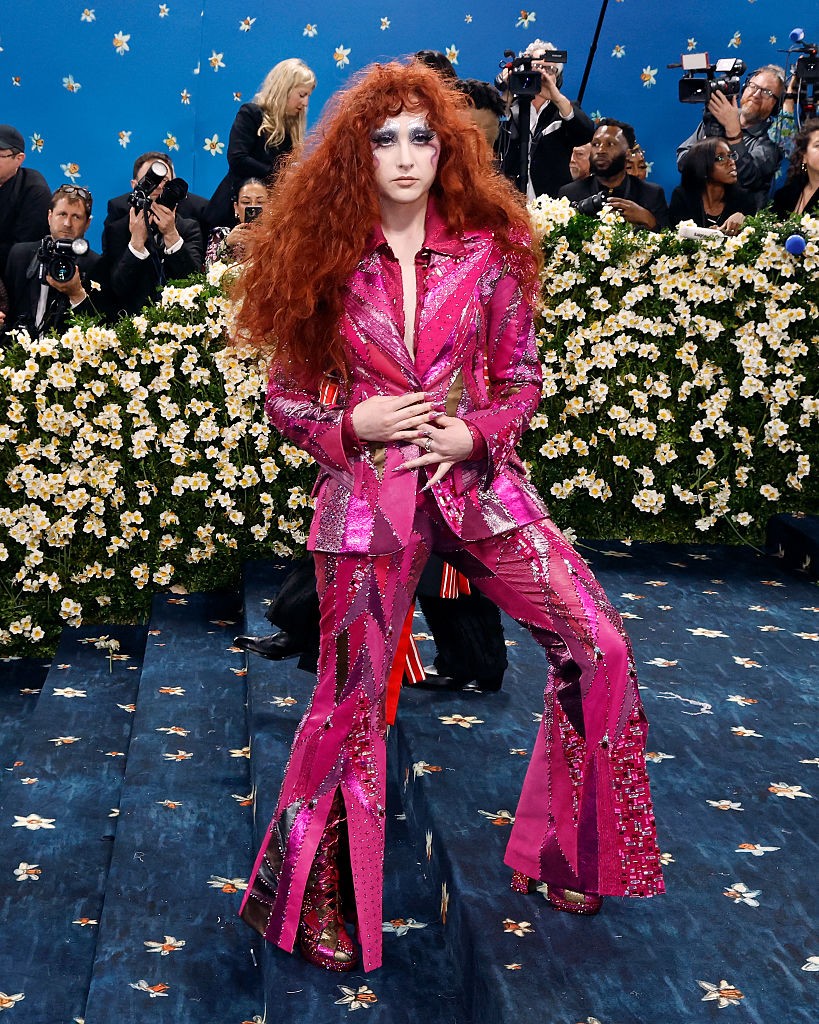 Chappell Roan – Paul Tazewell: A ragyogó rózsaszín, flitterekkel és patchwork részletekkel díszített Paul Tazewell-öltöny minden porcikájában vibrál, miközben a hetvenes évek glam-rock és dandy stílusát ötvözi egy kortárs queer esztétikával. A trapéznadrág, a látványos platformcipő és a színházi smink David Bowie és Ziggy Stardust világát idézi meg – erős, szabad, önazonos. Roan megjelenése nemcsak a tailoringről szól, hanem arról, hogy a stílus az önkifejezés egyik legfelszabadítóbb formája.