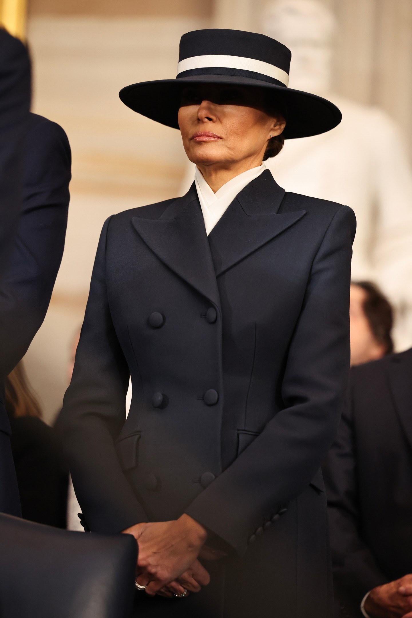 Melania Trump az amerikai tervezőkhöz való hűség jegyében Adam Lippes független tervező fekete kabátruháját, illetve egy hozzáillő széles karimájú Eric Javits kalapot viselt. Utóbbi bár kétségkívül elegáns, a megközelíthetetlenség szimbolikáját is közvetíti: többek szerint a first lady a férje csókját szerette volna elkerülni ezzel a divatválasztással.