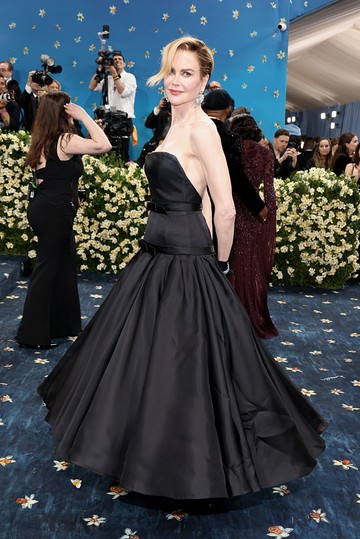 Nicole Kidman – Balenciaga: Nicole Kidman időtlen eleganciával vonult végig a 2025-ös Met-gála vörös szőnyegén, fekete Balenciaga Couture ruhájában. A fűzőszerű felsőrész és a bő, hercegnős szoknya klasszikus ballgown-sziluettet alkotnak, amit egy karcsúsító öv és diszkrét tailoring-elemek tesznek karakteressé. A megjelenést tovább fokozta új, két tónusú pixie-frizurája, amely finom kontrasztot teremtett az estélyi időtálló feketeségével. Kidman megjelenése maga volt az arisztokratikus dandyizmus női kiadása.