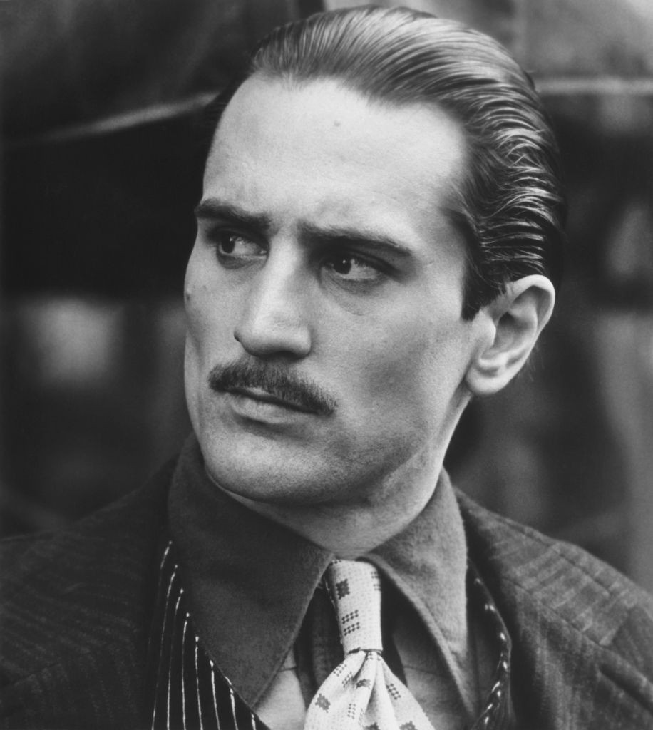Robert De Niro Vito Corleone szerepében, A Keresztapa II. (1974) című filmben. Francis Ford Coppola rendezésében Marlon Brando fiatalabb „előzményeként” tűnt fel, és ezzel a szereppel rögtön Oscar-díjat is nyert. A szigorú tekintet és a tökéletes korhű megjelenés mára klasszikussá vált.