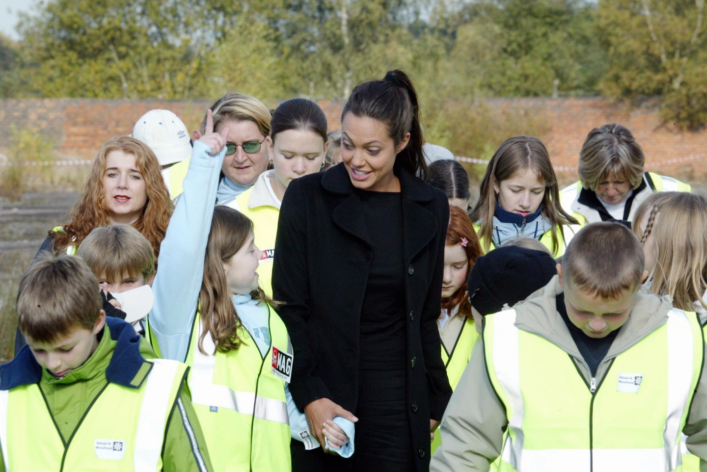 Ez a kép 2002. október 19-én készült az Egyesült Királyságban, Cheshire-ben, ahol Angelina Jolie az Adopt-A-Minefield nevű jótékonysági szervezetet támogatta. A világsztár aznap egy aknamentesítéssel foglalkozó tréningközpontot látogatott meg, ahol helyi iskolásokkal vett részt egy oktatási programban. A gyerekek a földalatti aknák veszélyeiről és az aknamentesítés folyamatáról tanulhattak.