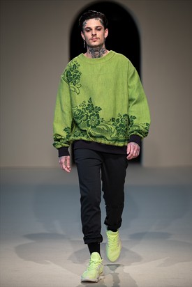 A bársonyos virágmotívumos applikációk vidéki jelleget kölcsönöznek a Laurus névre keresztelt pulóver modern szabásának, míg a gazdag zöld árnyalatok a természetet idézik. A pulóver anyagát körülbelül 80 évvel ezelőtt Magyarországon gyártották, és eredetileg gobelinre használták. Dora Zsigmond 2022 tavasz-nyár