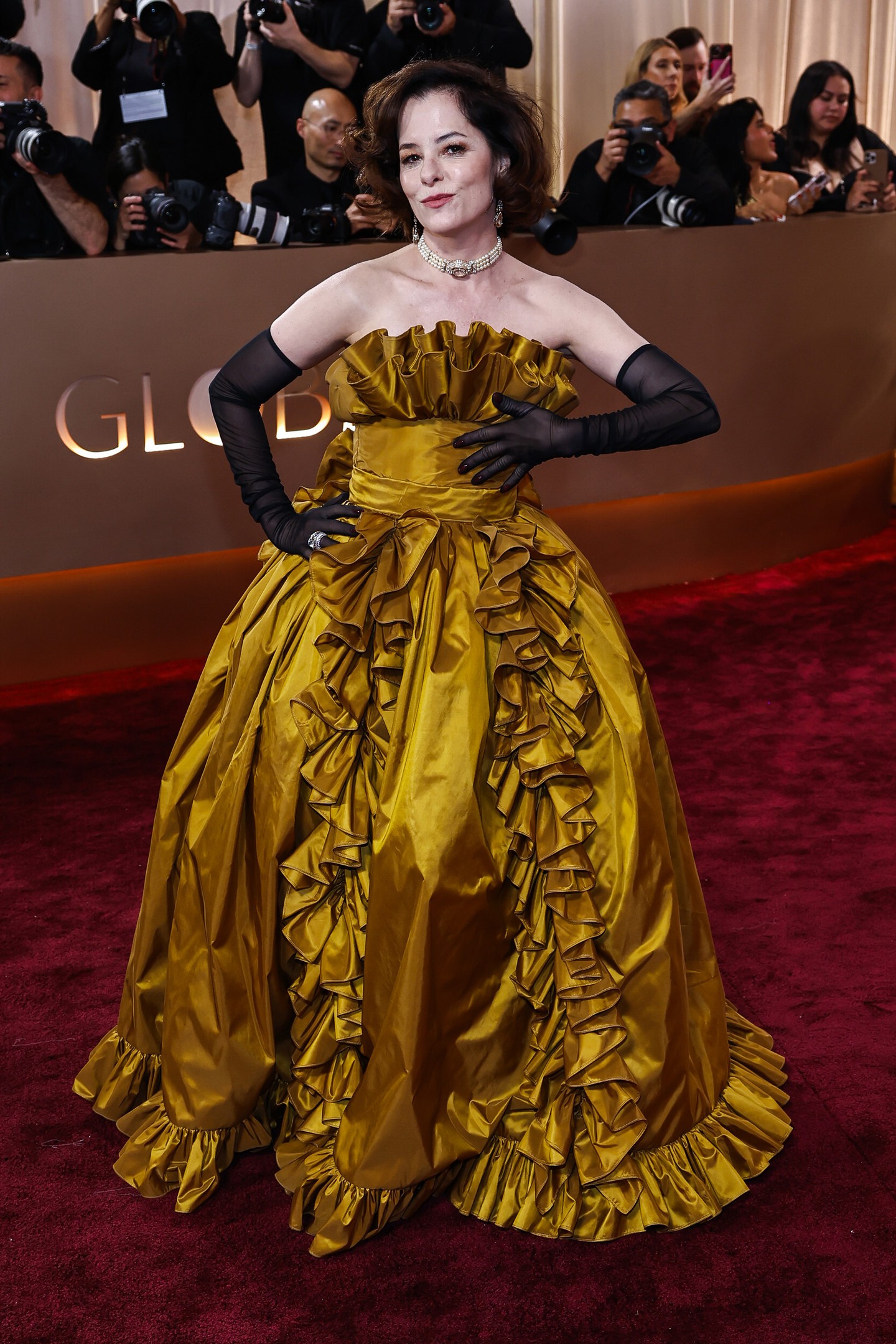 Az 57 éves Parker Posey pánt nélküli, fodros, arany Rodarte kreációjában királynőként tündökölt a Golden Globe vörös szőnyegén. A drámai hatást áttetsző, fekete kesztyűkkel fokozta. 