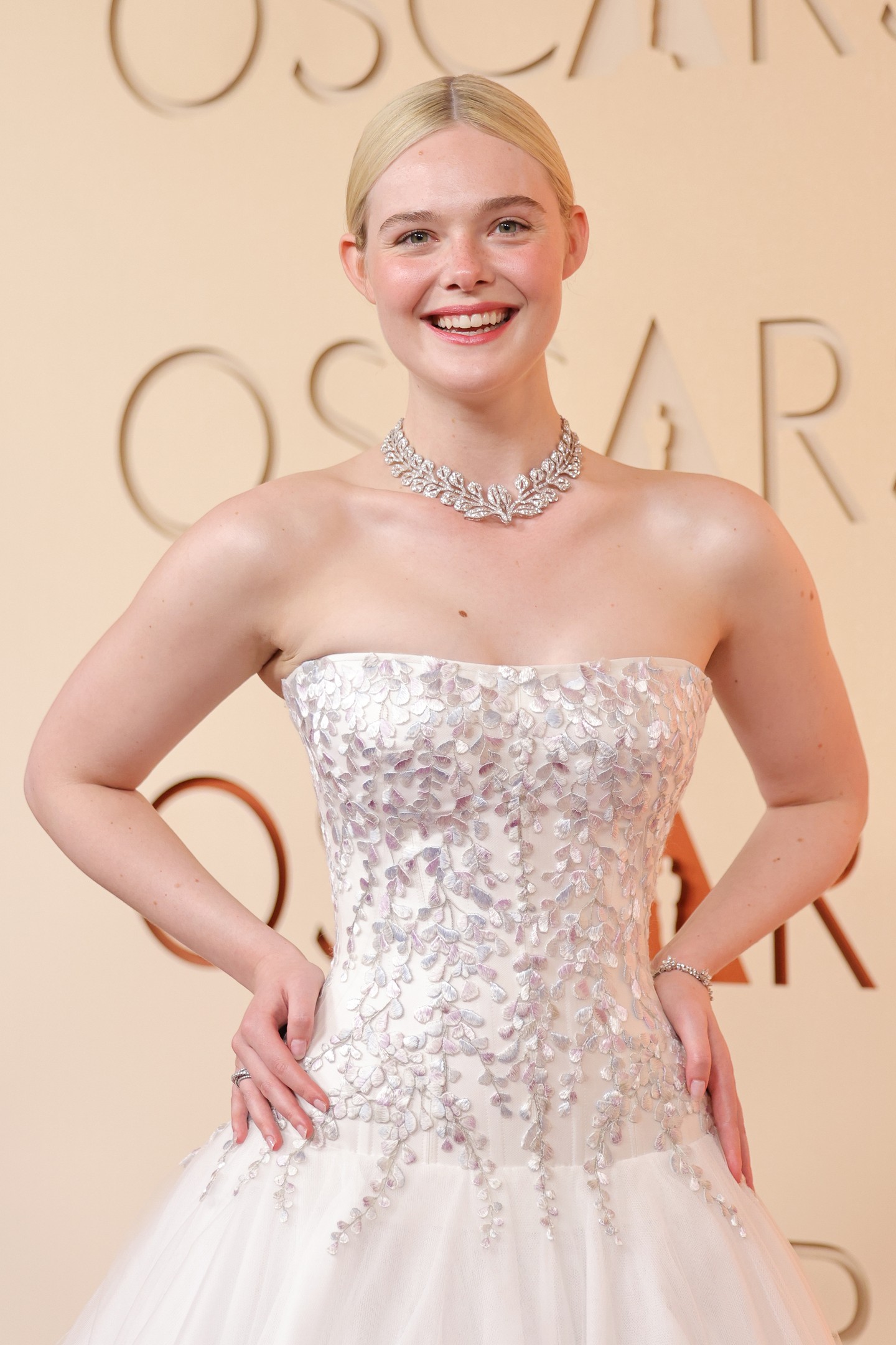 A ruha dekoltázsán és a szoknya alsó részén ezüst virághímzés díszelgett, melynek jelentése is volt. A fűzőben és a Cartier-ékszerekben is visszaköszönő finom akácmotívumot gyermekkori otthona ihlette. „Gyerekkoromban az otthonomban volt egy akácfa, ami tavasszal virágzott” – mesélte Fanning. „Emlékszem, azt gondoltam, hogy a legszebb dolog az, amikor a szirmok lehullanak, és felhőt hoznak létre a földön.” Burton és a Givenchy csapata ezt az emléket hímzéssé alakította: minden apró szirmot kézzel varrtak selyemszálakkal kék, rózsaszín, ezüst és lila árnyalatokban. 