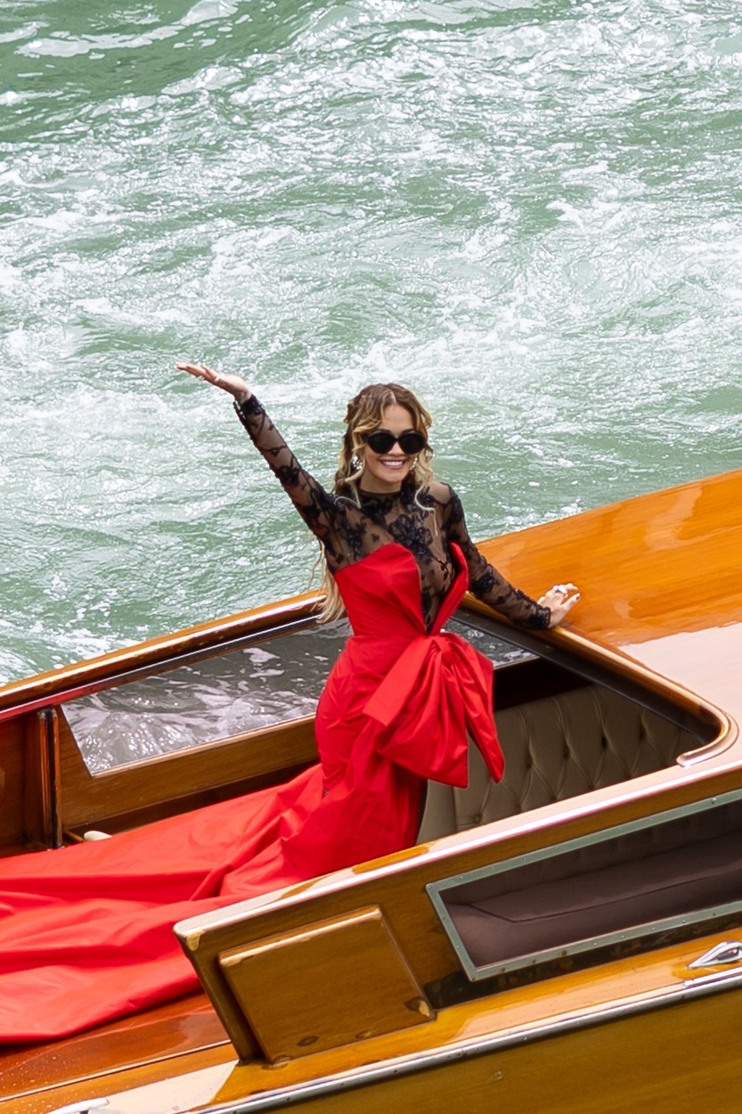 Rita Ora ezt követően extravagáns Moschino összeállításban szállt vízitaxiba – hosszú rúzspiros estélyi ruhája alatt áttetsző fekete csipke bodyt viselt, amely mellől a drámai napszemüveg és a játékos póz sem maradhatott el