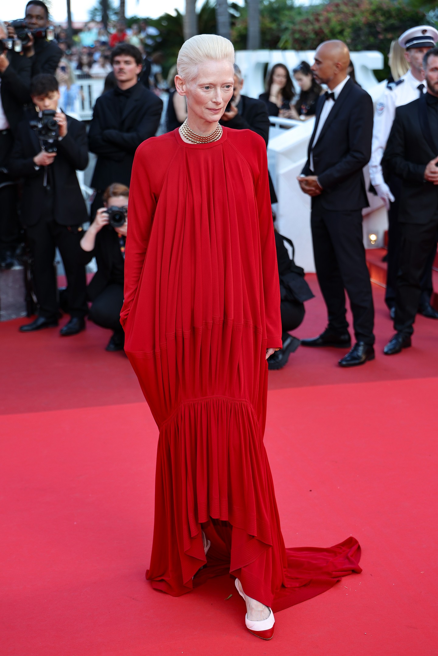Ami az öltözködést illeti, Tilda Swinton mindig elképesztően egyedi. A fesztivál utolsó estjére a színésznő egy piros ruhát választott a Chanel 2026-os őszi–téli kollekciójából. A hosszú ujjú, mélyen dekoltált ruha ívelt szegélye lágy, szokatlan vonalvezetést ad a darabnak. Az így kapott uszály rövid és lenge, messze eltér a cannes-i vörös szőnyegen megszokott hosszú, dívaszerű uszályoktól.