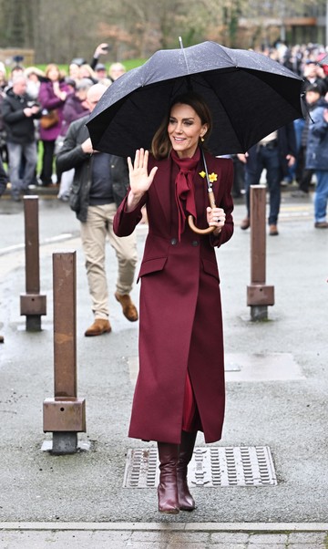 Amikor Katalinhercegné Wales-be látogatott, az esős napon is ragyogott. Egy bordó Alexander McQueen kabátot viselt Sarah Burton tervezőtől (ezt már 2024-ben is láthattuk rajta), amit szintén bordó, masnis blúzzal és bordó Gianvito Rossi csizmákkal egészített ki. 