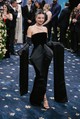 Miranda Kerr – Dior: Miranda Kerr megjelenése a Met-gálán a klasszikus elegancia és a kreatív szabászat tökéletes fúziója volt. A fekete bársony estélyi ruha sziluettje egyszerre idézte meg az old-school glamour és a tailoring világát: a ruha elején zakóként keresztbe hajtott rész és az abból kialakuló, drámai, földig érő ujjak a férfiöltöny ikonikus elemeit értelmezték újra nőies, szoborszerű formában. A gyöngyhálós nyaklánc, a kifinomult konty és a vörös rúzs igazi filmcsillag-hangulatot teremtett. Ez a megjelenés minden részletében a „Tailored For You” szellemiségét tükrözte – finoman, de határozottan.