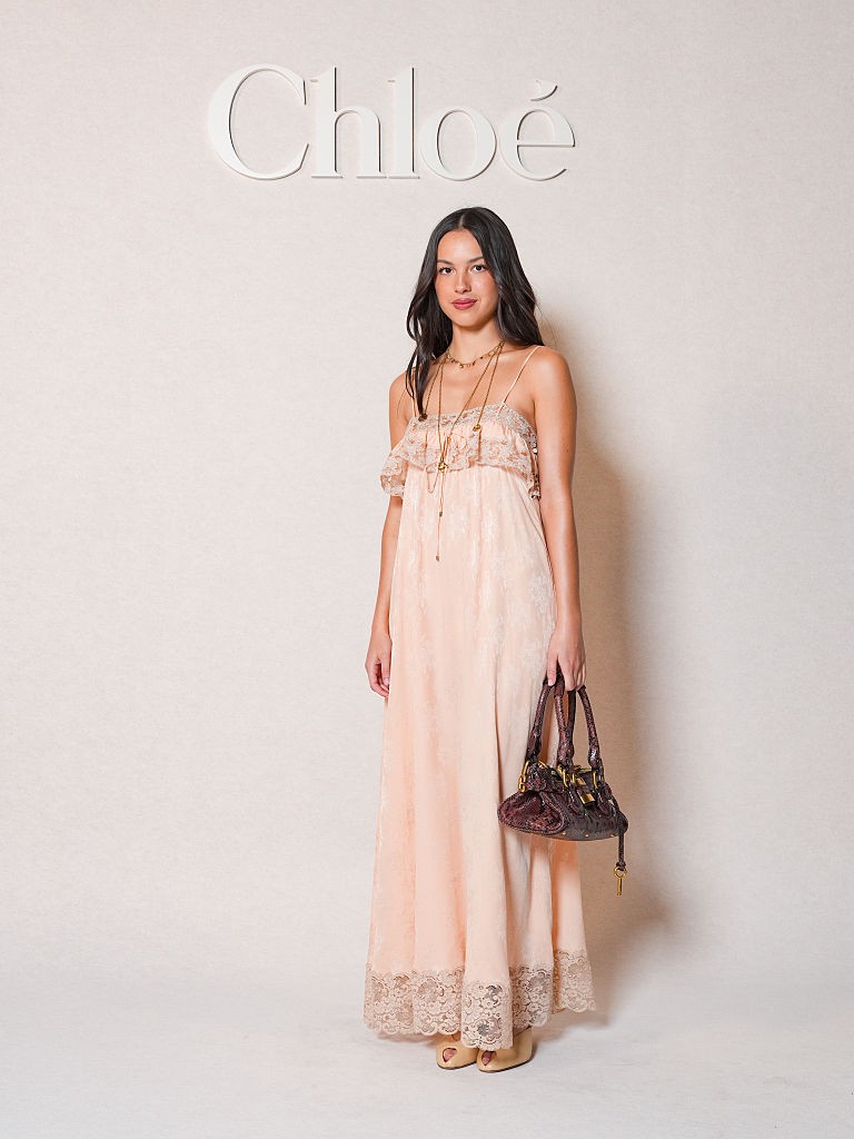 Olivia Rodrigo a Chloé fashion show-ján vett részt egy spagettipántos, halvány rózsaszín, csipkével díszített maxi ruhában. 