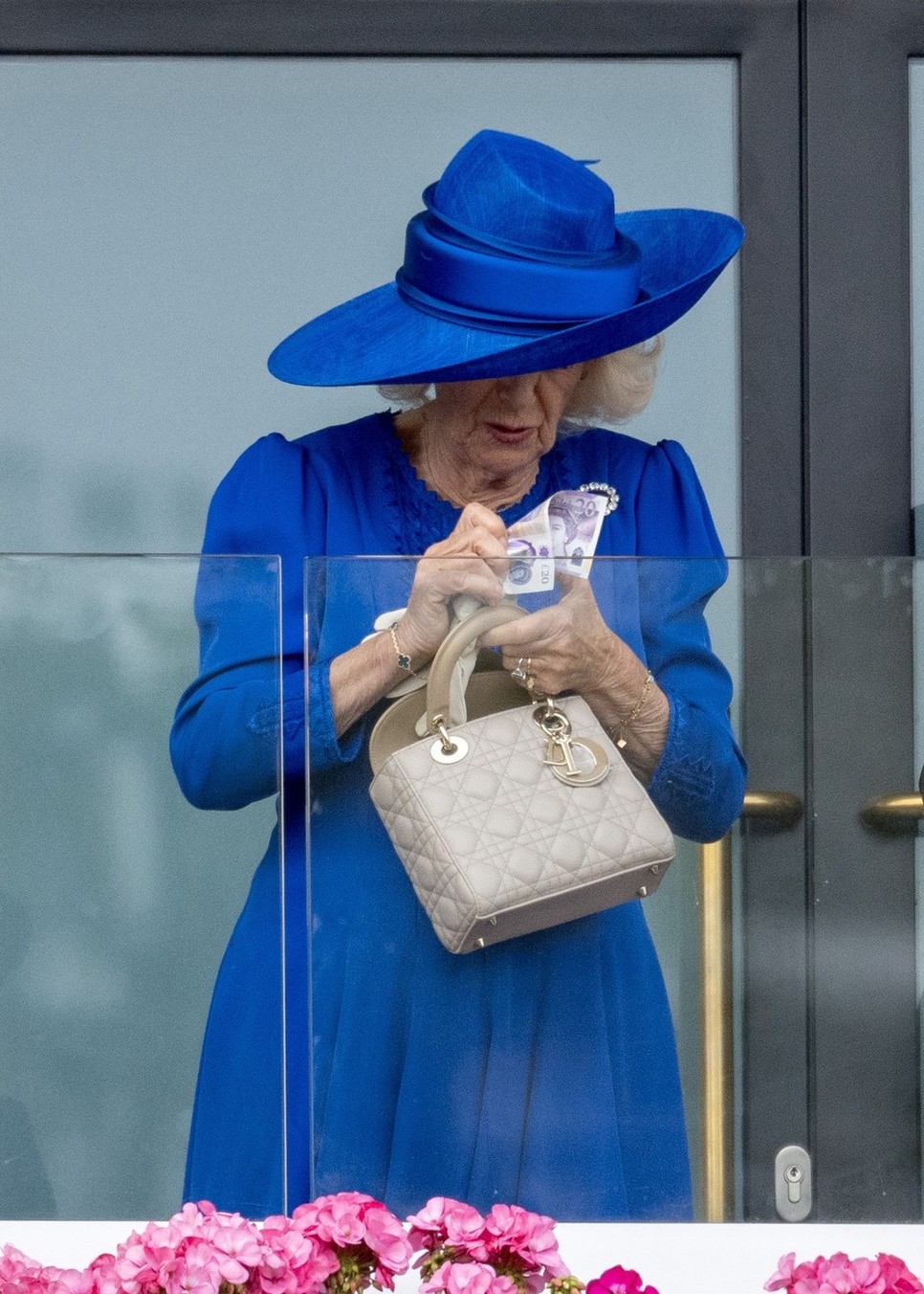 Kamilla királyné egy bankjeggyel a kezében a Royal Ascoton