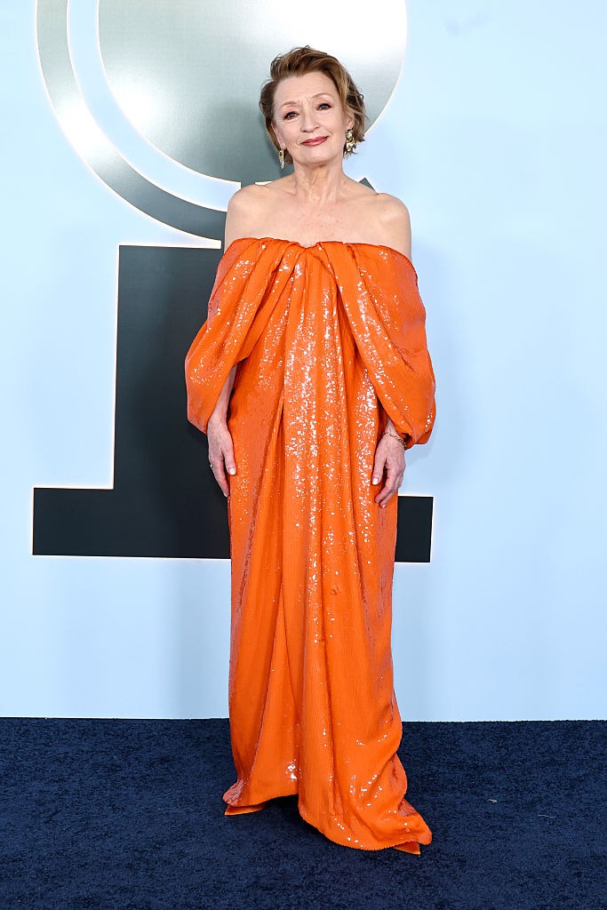 Lesley Manville valósággal ragyogott ebben a vibráló, élénknarancssárga estélyiben. A 70 éves színésznő egy ejtett vállú, földig érő kreációt választott, amelyet a tetőtől talpig csillogó flitterek és a finom, lágyan omló drapériák tettek igazán különlegessé. A ruha laza, mégis elegáns sziluettje tökéletesen passzolt a gála ünnepi hangulatához, a látványos és merész színválasztás pedig garantálta, hogy minden tekintet rászegeződjön.