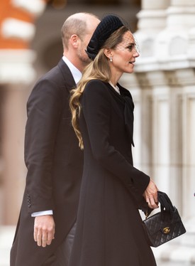 Ezt a Catherine Walker kabátot nem először láthatjuk Katalin hercegnén. A  letisztult darabot egy Jane Taylor-féle pillbox kalappal párosította, amelyen egy finom fátyol is helyet kapott. A klasszikus megjelenést a tökéletes Chanel táska tette teljessé.