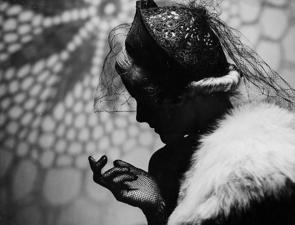 Santhó Imre egyik ikonikus divatfotója az 1930-as évekből, amely a fény és árnyék játékával emeli ki a női elegancia modern formáit. A Capa Központ „Elegancia és kísérletezés” című kiállítása új fénybe helyezi a fotográfus elfeledett életművét