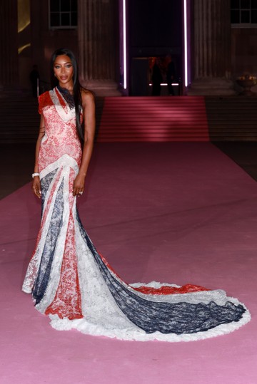 Naomi Campbell lélegzetelállító, testhezálló Givenchy-ruhában érkezett, amely a 2000-es őszi/téli Couture kollekció egyik archív darabja. A brit zászló színeiben pompázó csipkeruha aszimmetrikus vállmegoldásával és drámai uszályával tökéletesen egyesíti a klasszikus couture eleganciát a modern, ikonikus megjelenéssel.