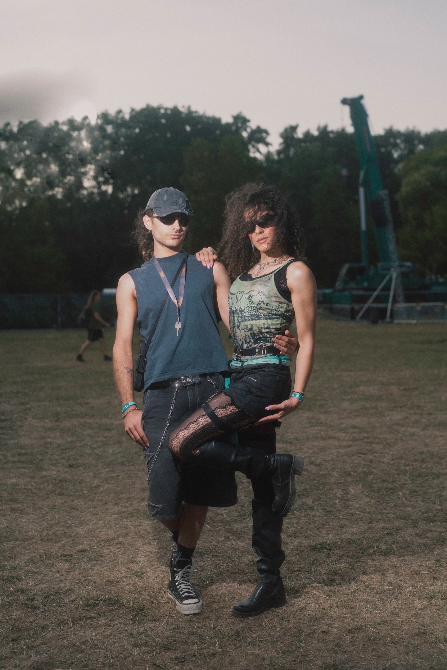 A fotón látható összeállítás egy kortárs, alternatív fesztiválstílust idéz, amely a 2000-es évek eleji grunge és industrial hatásokat modern rave- és DIY-elemekkel ötvözi. A fiú megjelenése a kilencvenes évek végi skate-punk világát idézi, míg a lány szettje a 2010-es évek eleji cyber-goth és alternatív klubkultúra inspirációját hordozza, amelyet a futurista napszemüvegek tesznek teljessé.