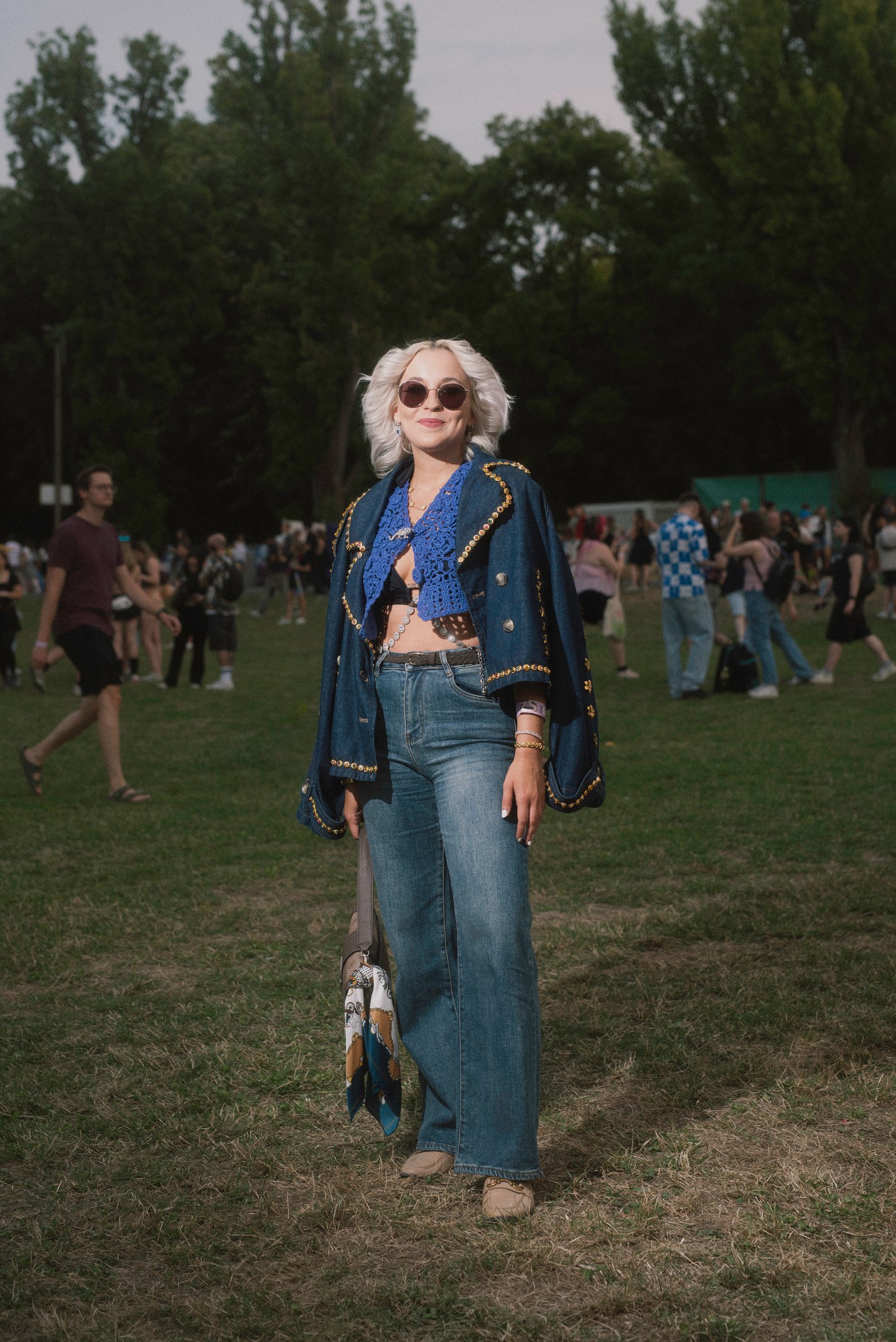 Ez a szett szintén erősen megidézi a ’70-es évek bohém, fesztiválhangulatú stílusát, méghozzá modern csavarral. A kék horgolt felső és a bő szárú farmer a korszak ikonikus darabjai, amelyeket a díszes, arany szegecsekkel szegélyezett farmerdzseki még inkább a vintage irányba lendít. A napszemüveg, a táskára kötött sál és a finom ékszerek mind hozzájárulnak ahhoz a gondtalan, mégis tudatosan összeállított megjelenéshez, amely egyszerre nosztalgikus és friss.