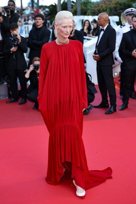 Ami az öltözködést illeti, Tilda Swinton mindig elképesztően egyedi. A fesztivál utolsó estjére a színésznő egy piros ruhát választott a Chanel 2026-os őszi–téli kollekciójából. A hosszú ujjú, mélyen dekoltált ruha ívelt szegélye lágy, szokatlan vonalvezetést ad a darabnak. Az így kapott uszály rövid és lenge, messze eltér a cannes-i vörös szőnyegen megszokott hosszú, dívaszerű uszályoktól.